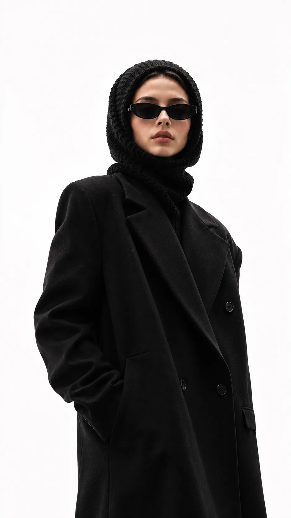 Contemporary editorial portrait of a fashionable woman in a knitted headpiece and oversized black clothing with luxury studio lighting.