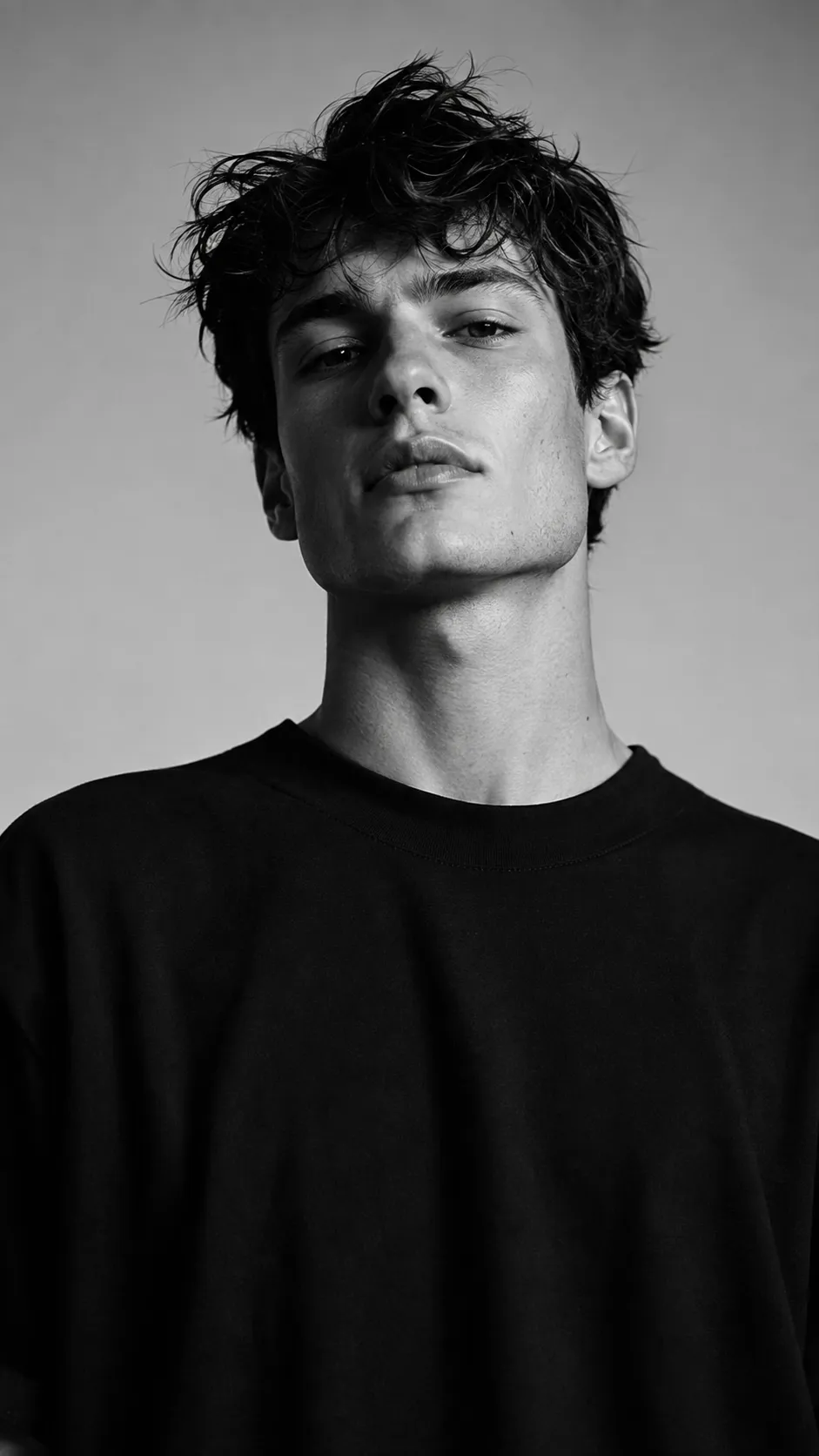 Black and white cinematic male portrait with messy hair and minimalist black fashion